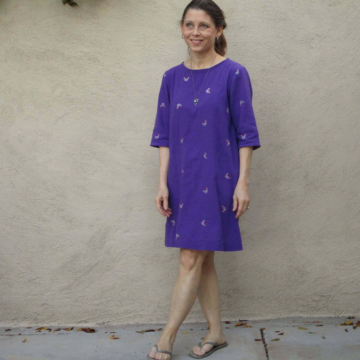 Woman wearing a purple dress with butterfly prints, showcasing the Whisper blouse Paper Pattern design.