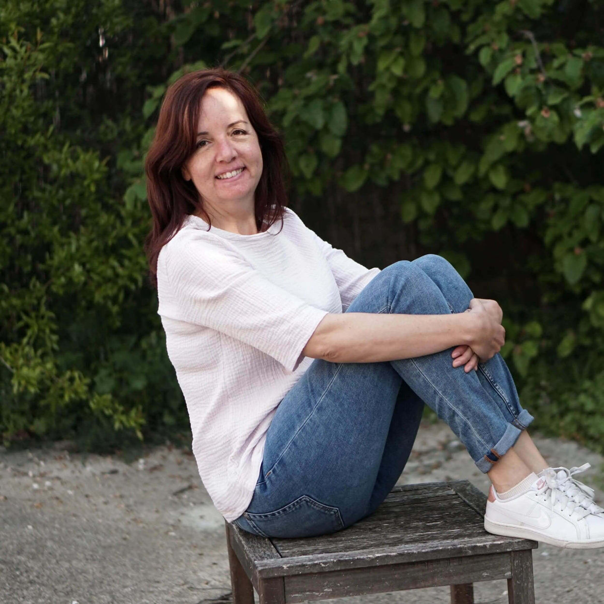 Woman wearing a Whisper blouse Paper Pattern sitting on a wooden bench in casual attire outdoors.