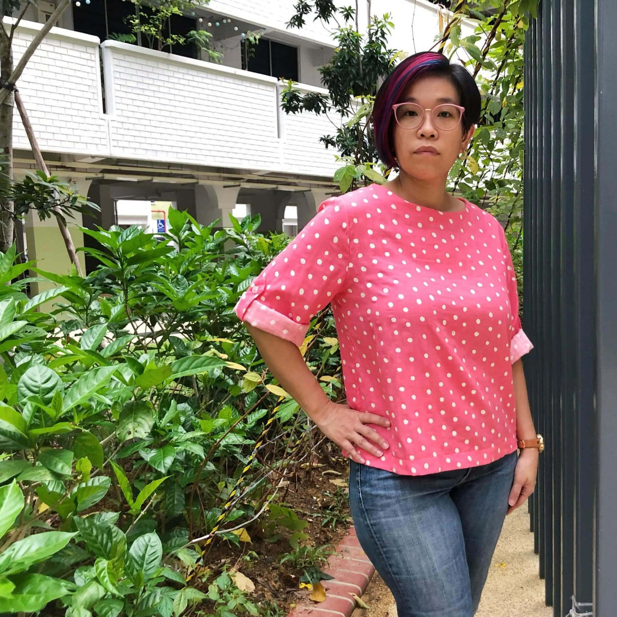 Woman wearing a pink polka dot shirt made from the Whisper blouse Paper Pattern in a garden setting.
