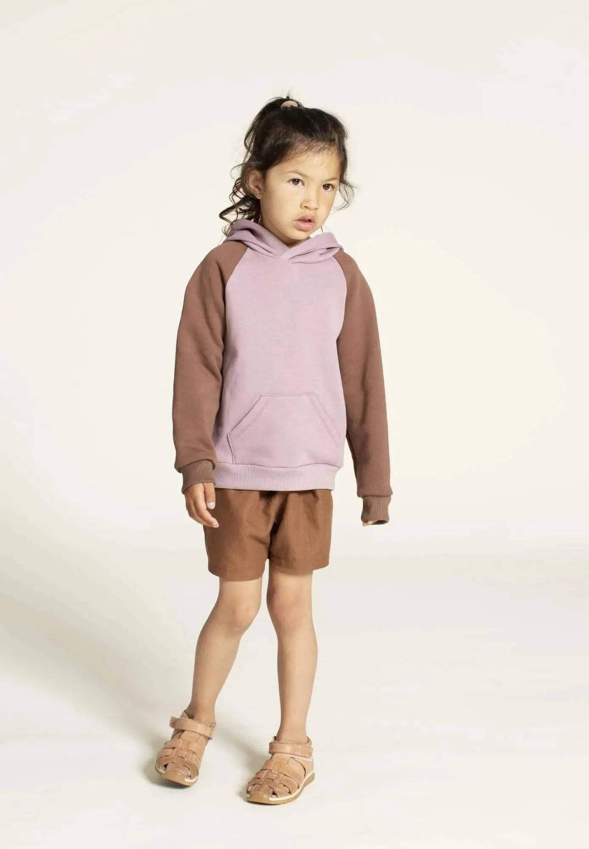 Hoodie sweater sewing pattern for kids showcased on a girl wearing a pink and brown hoodie with shorts.