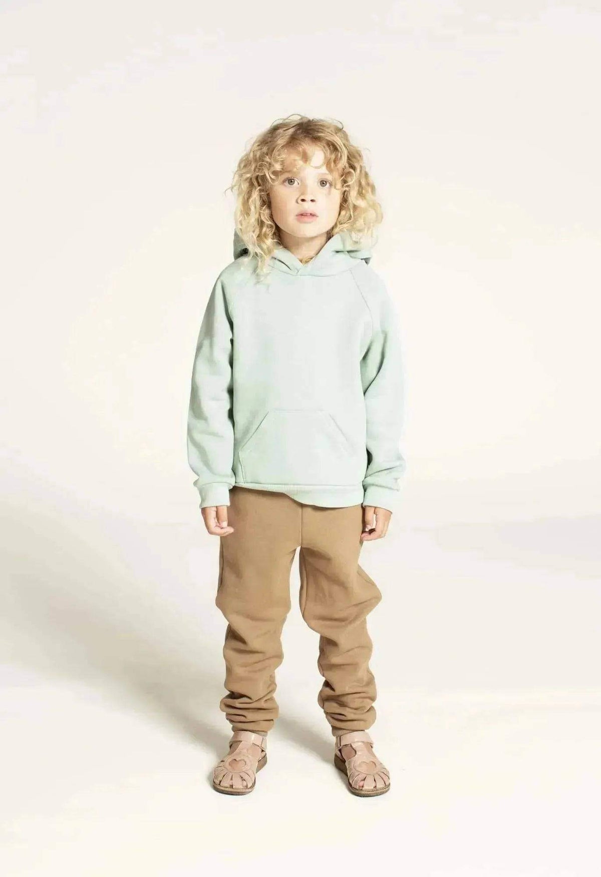 Hoodie sweater sewing pattern for kids, featuring a child in a mint green hoodie and stylish brown pants.