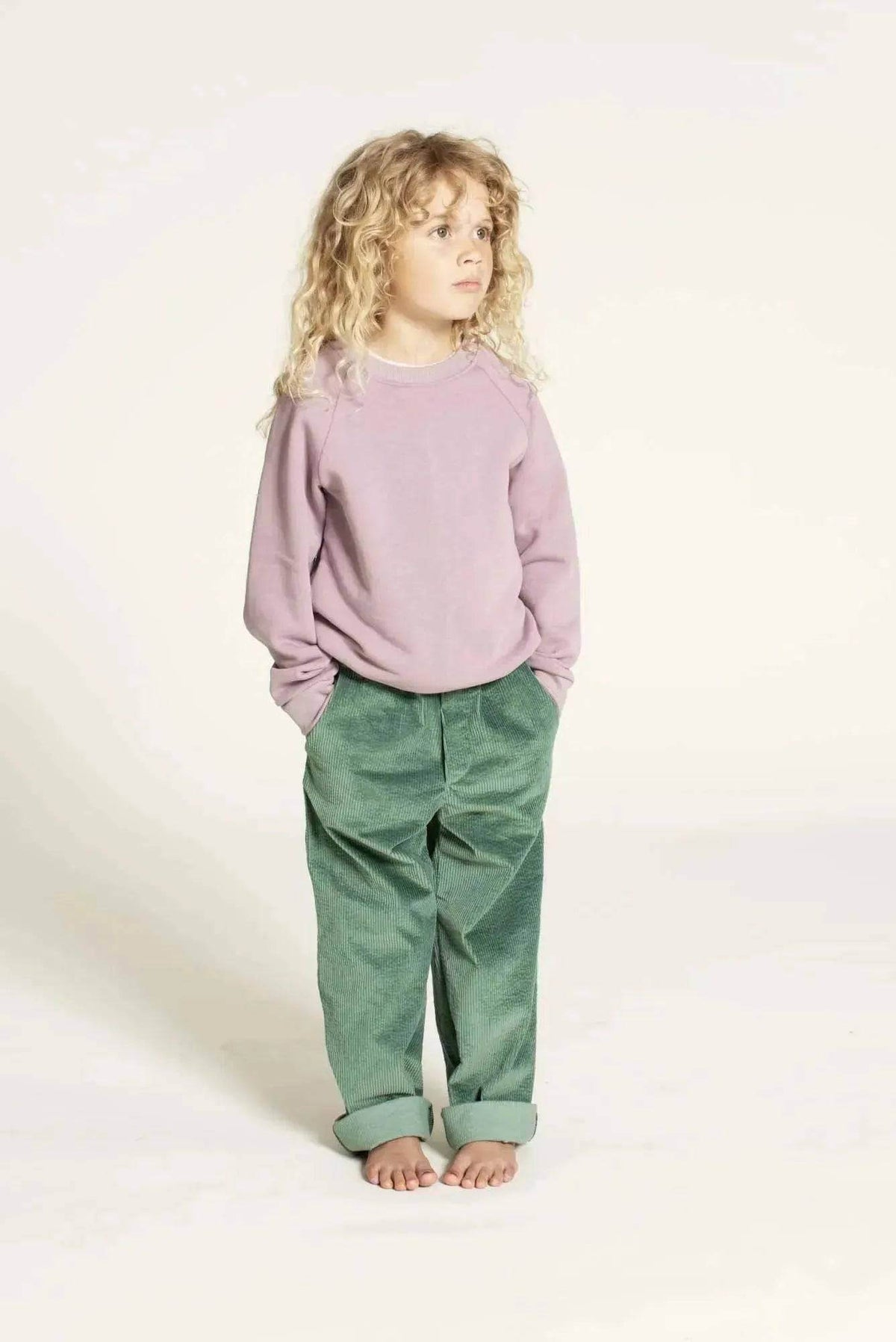 Child wearing a pink sweatshirt and green pants, showcasing a casual look, perfect for showcasing the Hoodie sweater sewing pattern.