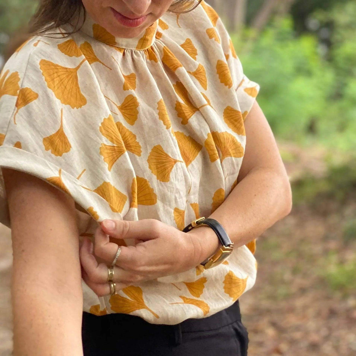 Woman wearing a light floral shirt showcasing the Tulip Top Paper Pattern with gathered neckline and dolman sleeves.